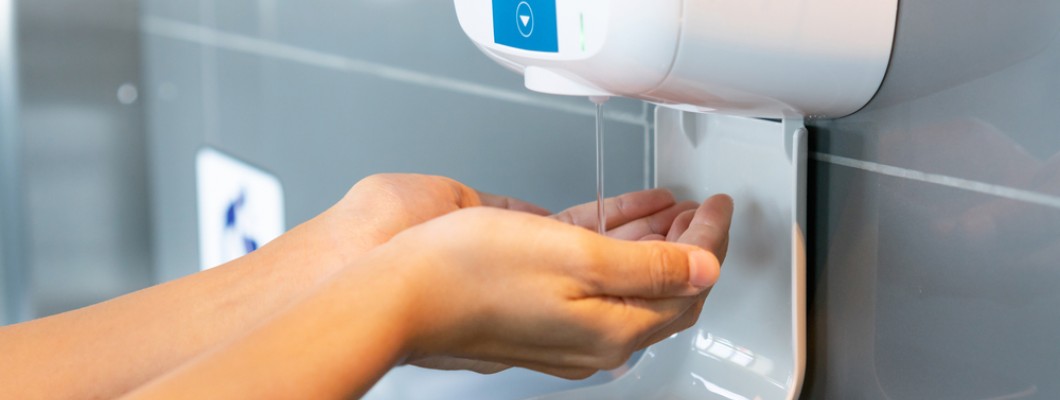 femeie care isi dezinfecteaza mainile la un dispenser automat