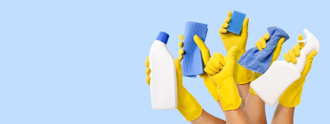 produse esențiale pentru curățenie: mănuși, lavete, spray și soluții de curățare ținute în mâini pe fundal albastru